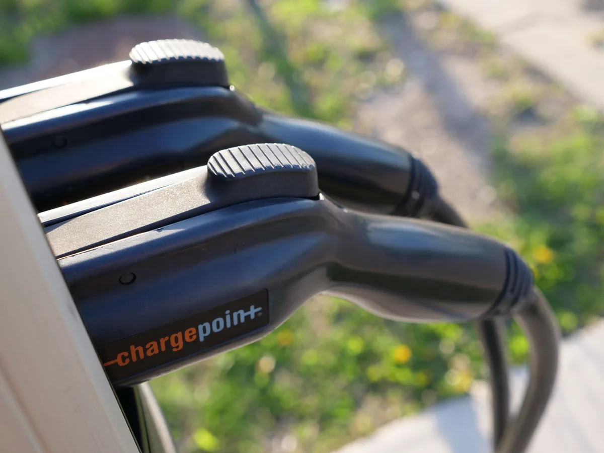 Personne branchant un chargeur sur la batterie d'un vélo électrique (vue anonyme)